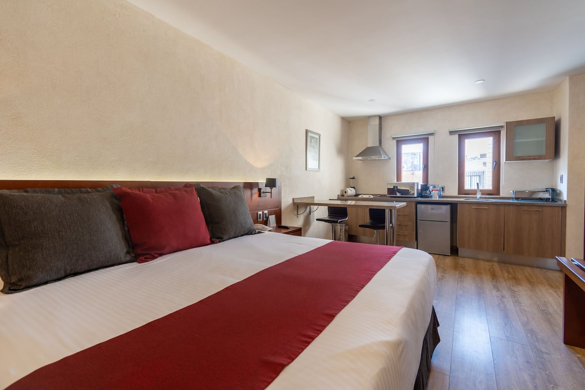 A hotel room with a large bed, a kitchenette, and a view of the city.