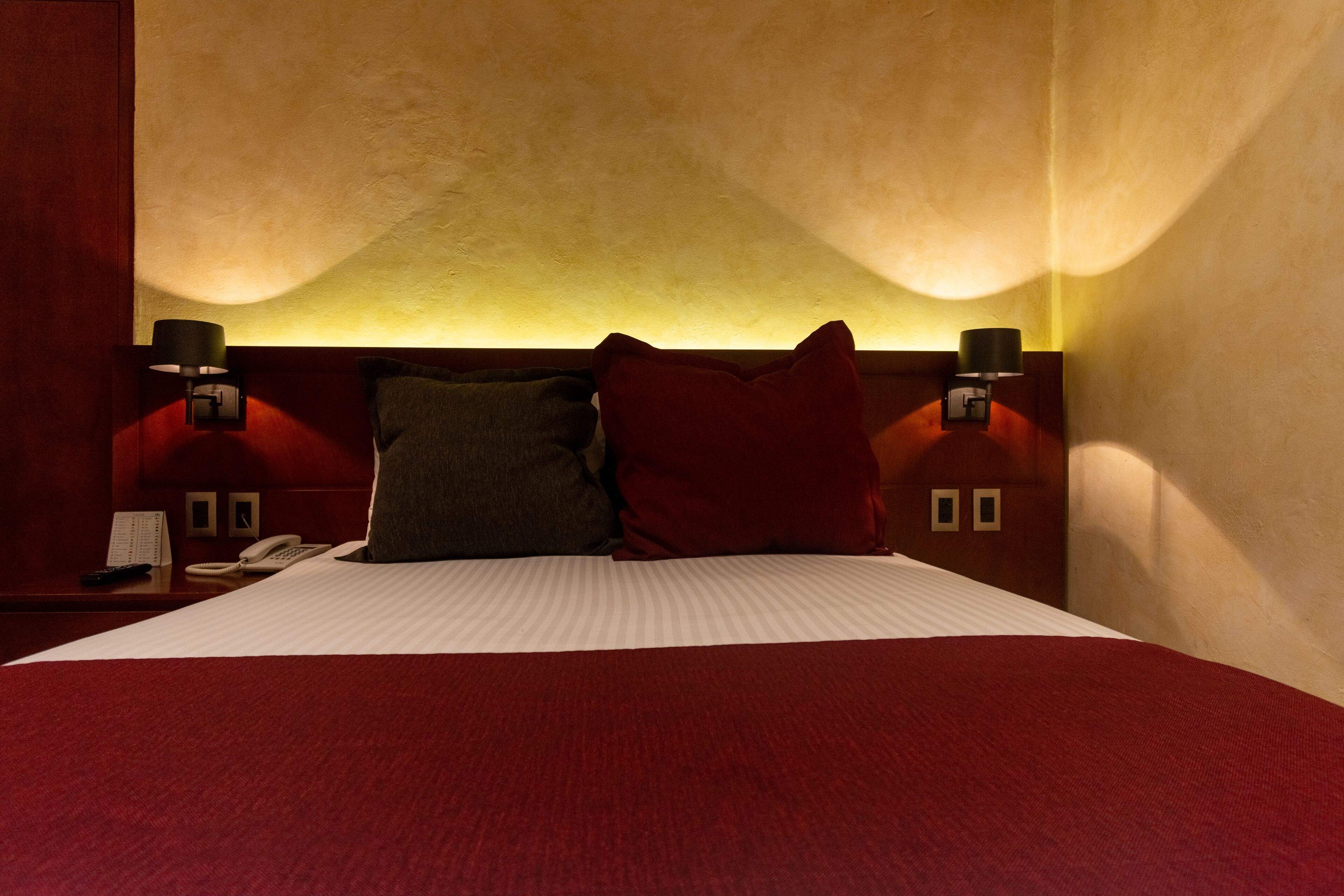 Een hotelkamer met een groot bed, twee bedlampjes, een nachtkastje met een telefoon en een wandlamp.