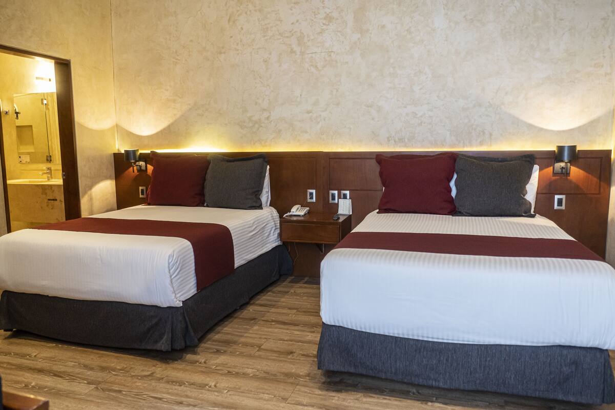 A hotel room with two beds, wooden flooring, and a wooden headboard.