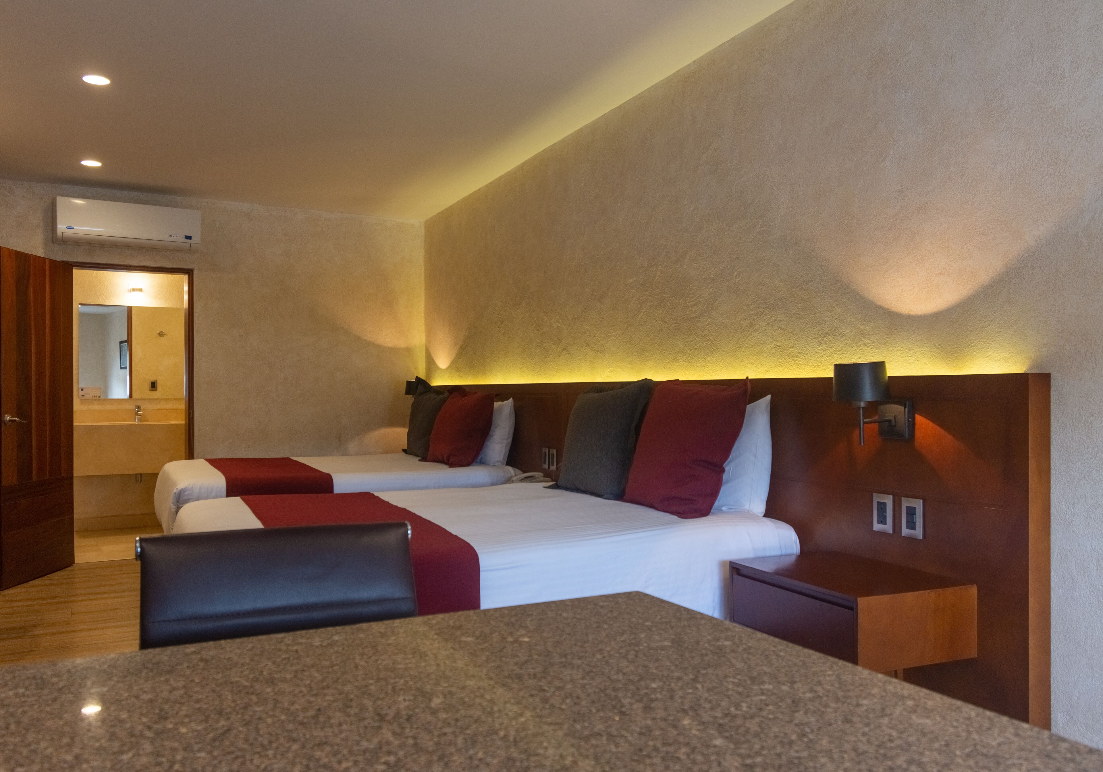 A hotel room with two beds, a wooden headboard, a granite countertop, and a wall-mounted air conditioner.