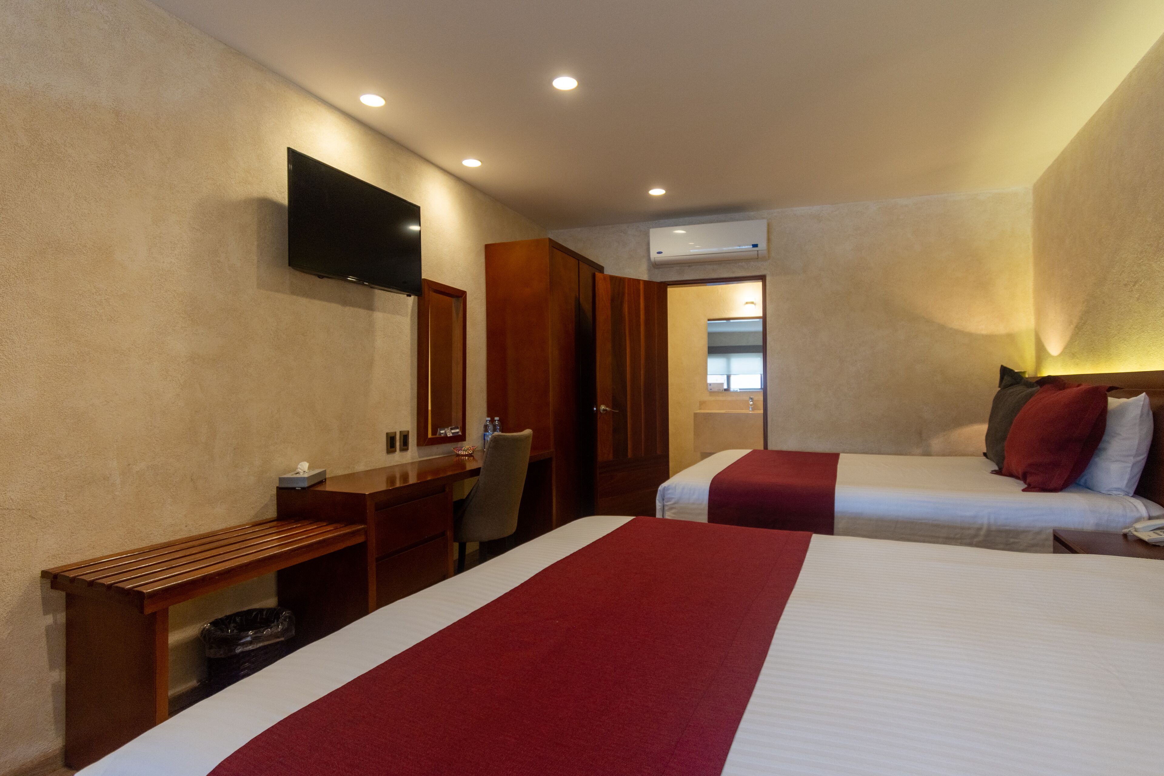 Habitación de hotel con dos camas, un escritorio, una silla, un televisor y un equipo de aire acondicionado.