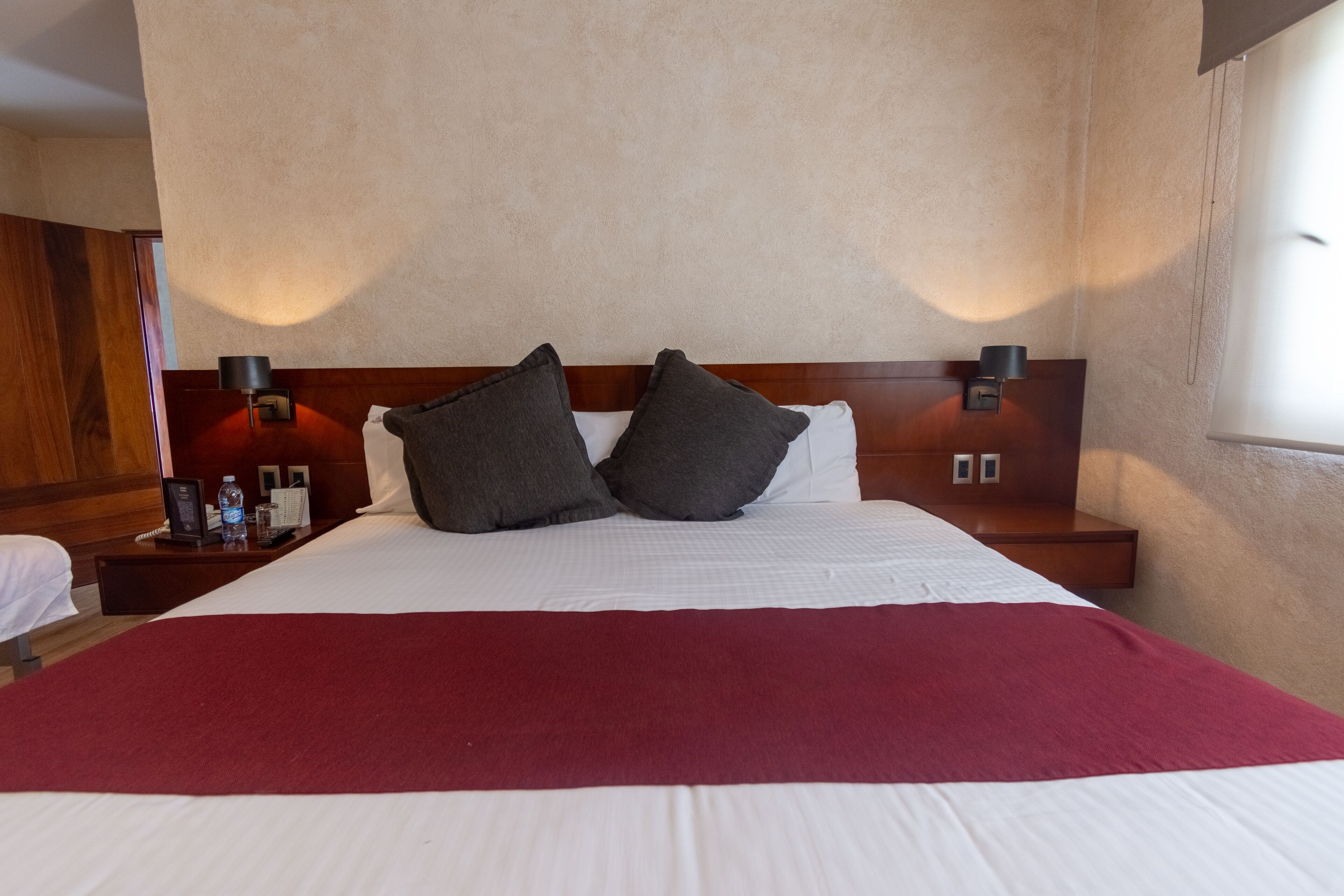 Een hotelkamer met een groot bed, twee nachtkastjes, een rode plaid en een houten hoofdeinde.