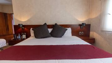 Een hotelkamer met een groot bed, twee nachtkastjes, een rode plaid en een houten hoofdeinde.