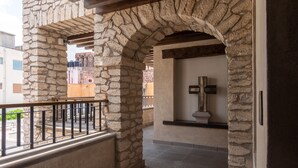 Un pasillo de piedra con barandilla, que conduce a una habitación con pared de piedra y una cruz en un estante.
