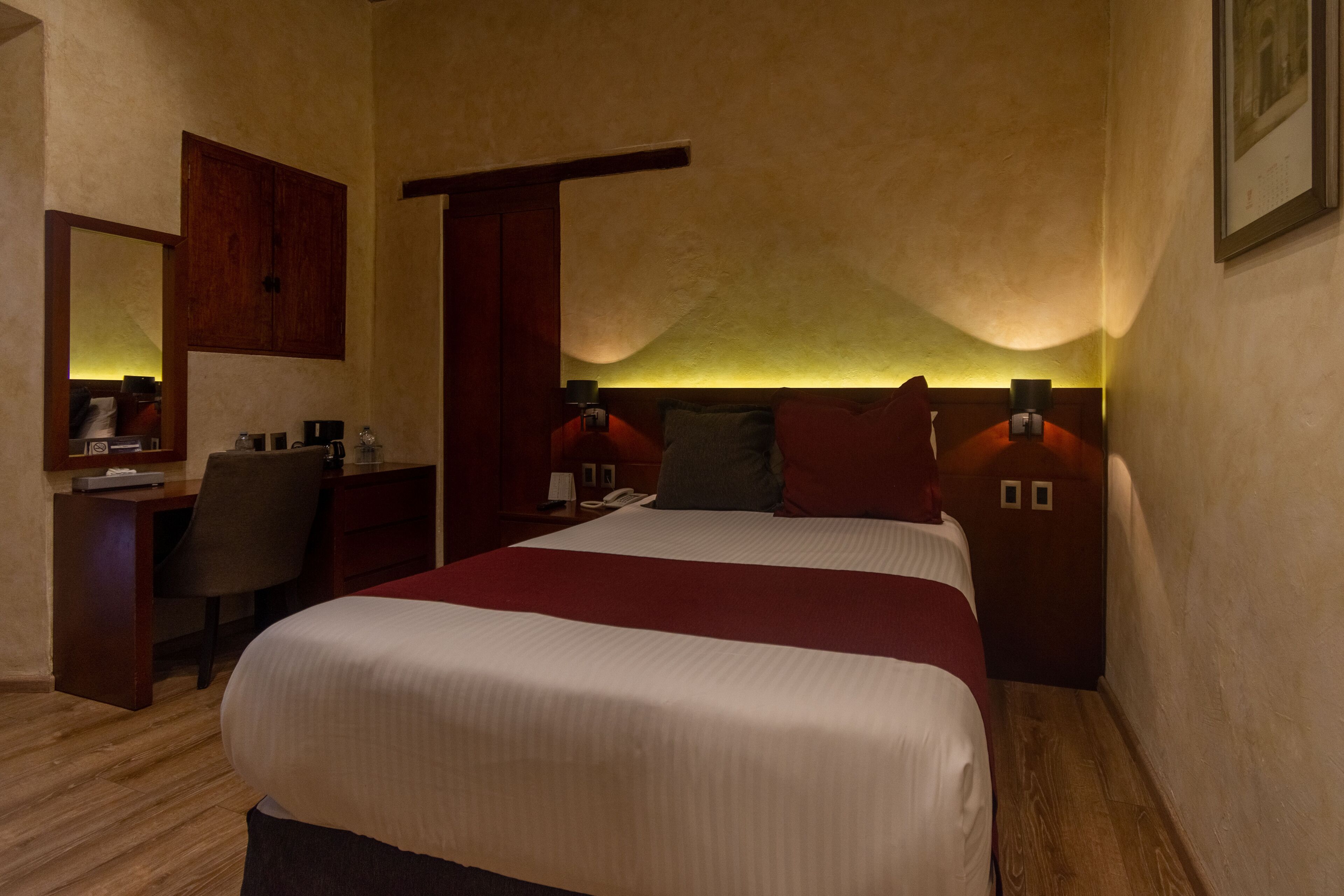 A hotel room with a large bed, a desk, a chair, a wardrobe, and a mirror.