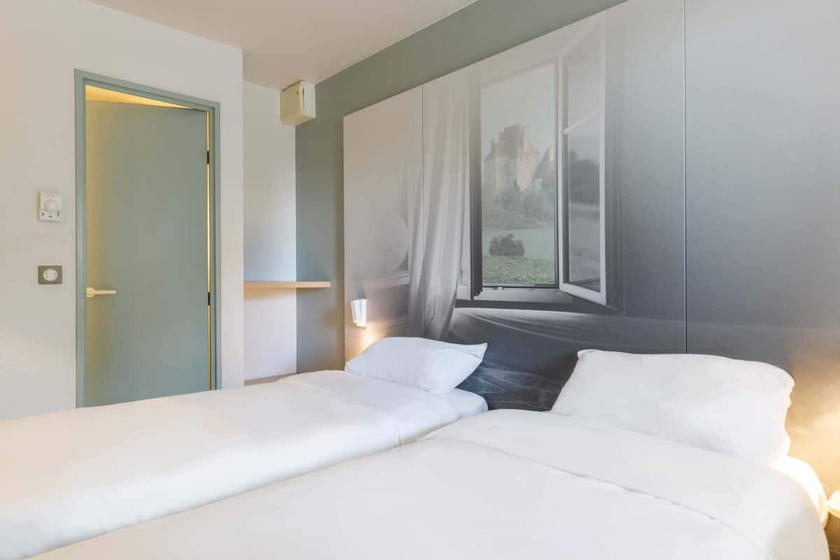 A hotel room with a bed, a window with a view of a castle, and a door.