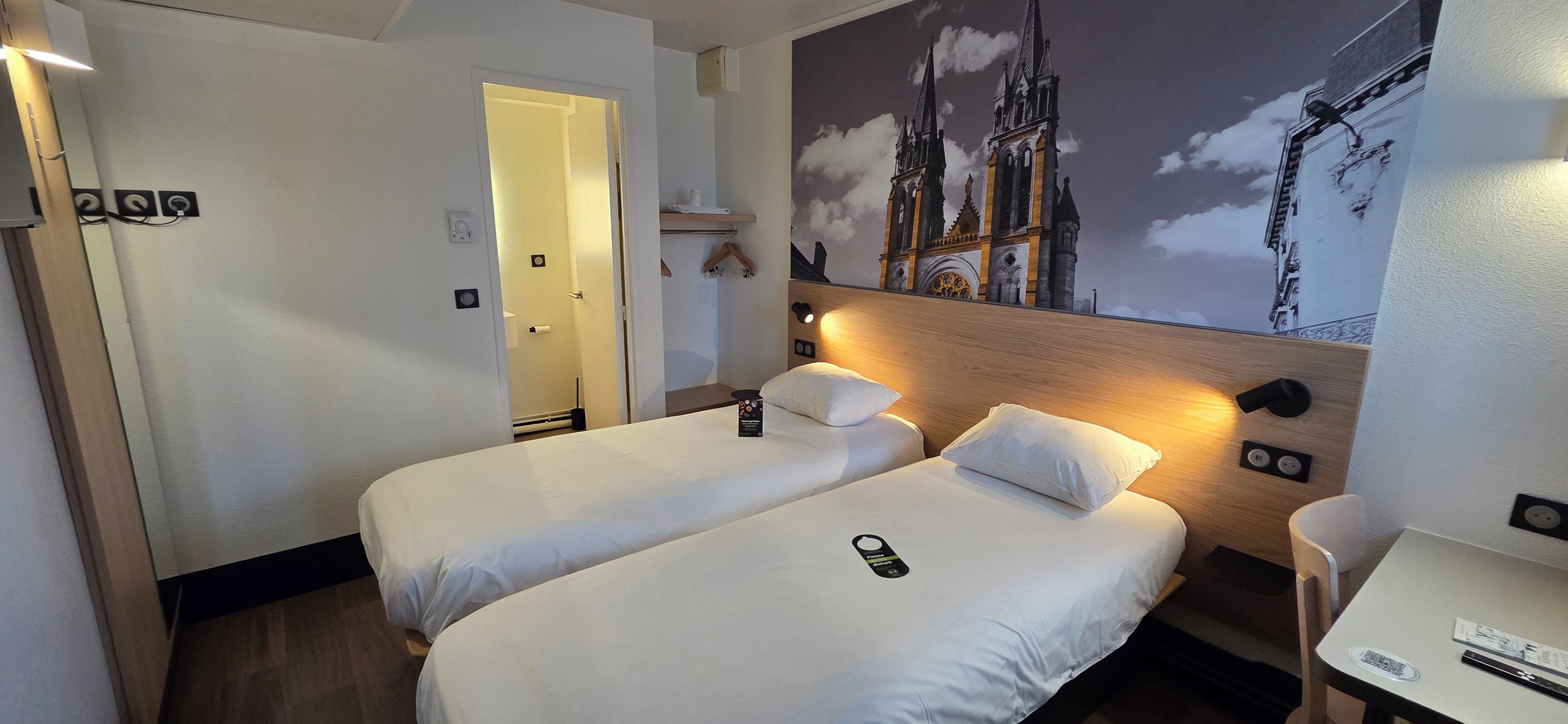 Habitación de hotel con dos camas, un escritorio y un mural de una catedral.