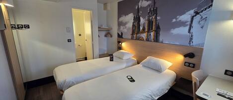 Habitación de hotel con dos camas, un escritorio y un mural de una catedral.
