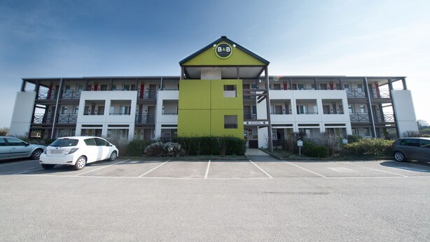 A multi-story building with a green and white facade, a parking lot in front, and a sign indicating a business or office space. - B&B HOTEL Moulins Toulon‑sur‑Allier (Toulon-sur-Allier)