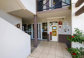 Entrada de hotel con mostrador de recepción, mesa de seguridad y escalera que conduce a un nivel superior.