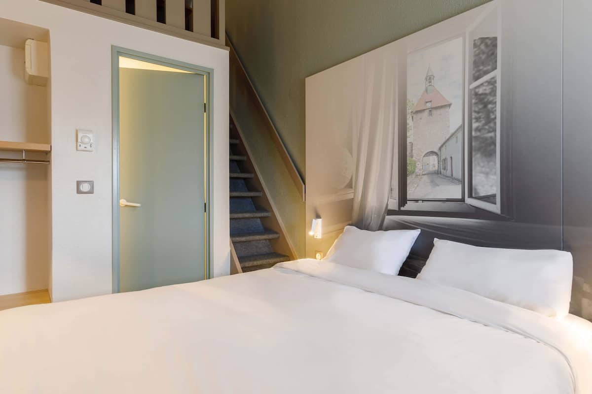 A hotel room with a bed, a staircase, a door, and a wall-mounted picture.