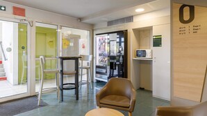 A reception area with a brown leather chair, a small round table, a refrigerator, and a vending machine. - B&B HOTEL Moulins Toulon‑sur‑Allier (Toulon-sur-Allier)