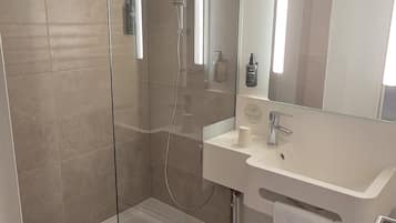 Een moderne badkamer met een douchecabine van glas, een wit wastafelmeubel en een grote spiegel.