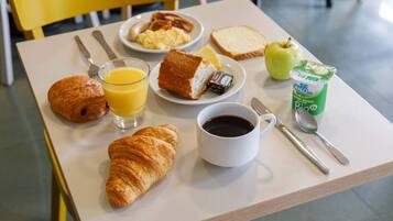 Taula de petit esmorzar amb croissants, torrades, ous, becon, suc, cafè i un envasament de iogurt.