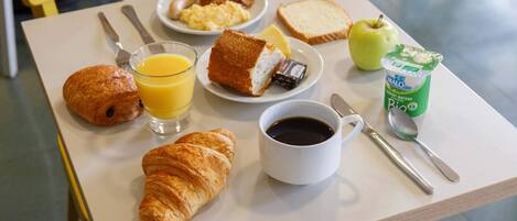 A breakfast table with croissants, toast, eggs, bacon, juice, coffee, and a yogurt container.