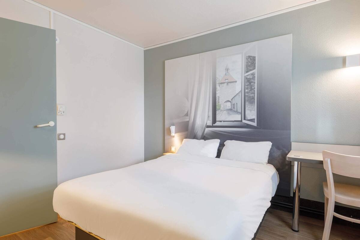 A hotel room with a large bed, a desk, and a chair.