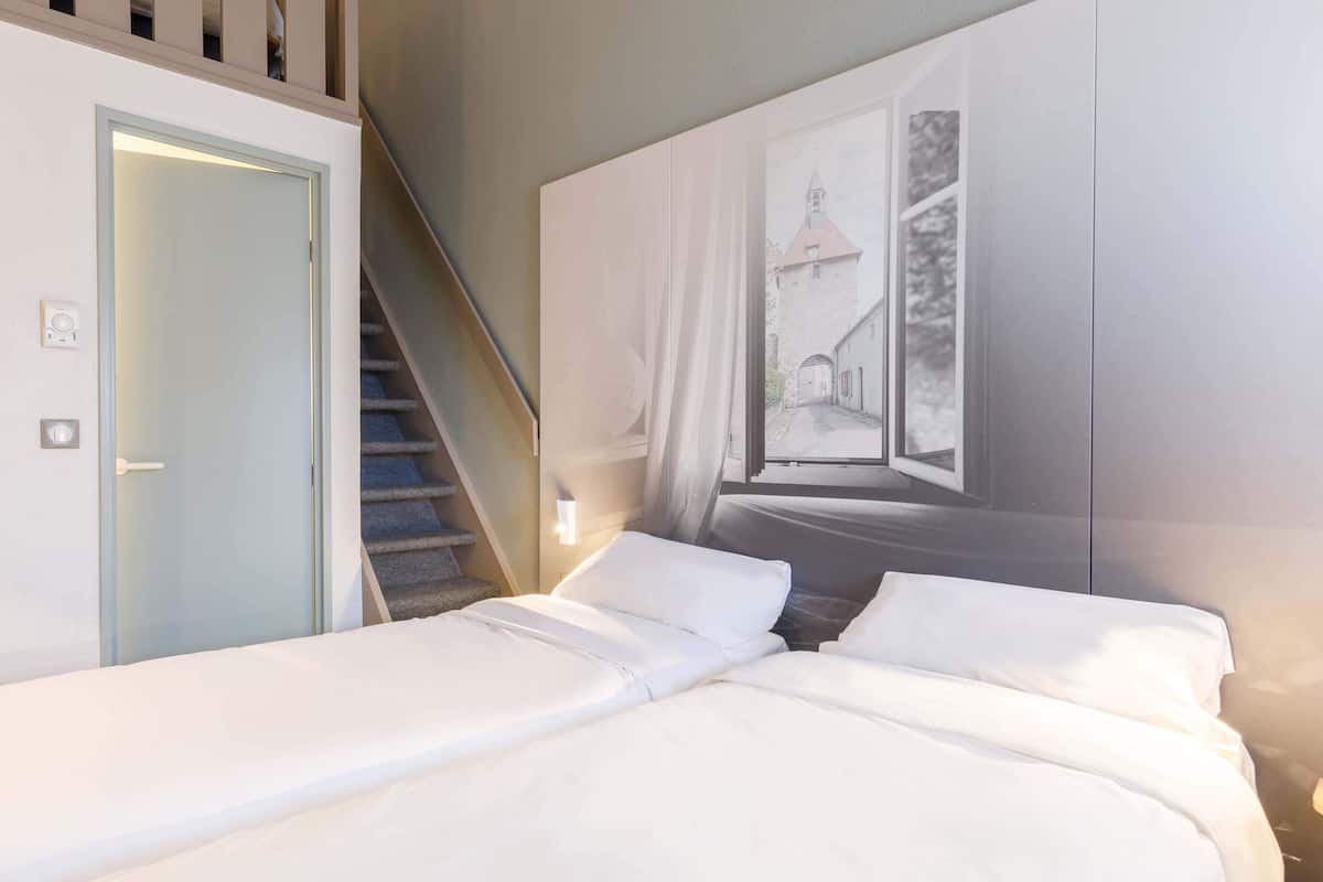A hotel room with a bed, a staircase, and a wall-mounted artwork depicting a street scene.