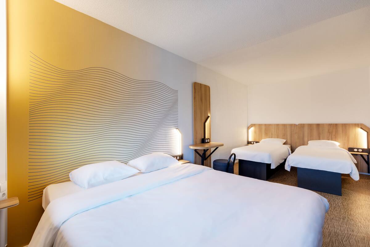 Une chambre d’hôtel avec un grand lit, deux tables de chevet, une petite table et un mur orné d’un motif ondulé.