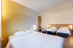 Habitación de hotel con una cama grande, dos camas más pequeñas, un cabecero de madera, mesitas de noche y una pared con un diseño ondulado.