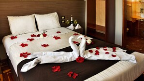 A hotel room with a neatly made bed, a wooden headboard, a nightstand with a bottle and glasses, and a bathroom visible through an open door.