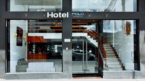 A hotel entrance with a glass facade, a visible reception area, and a staircase leading inside.