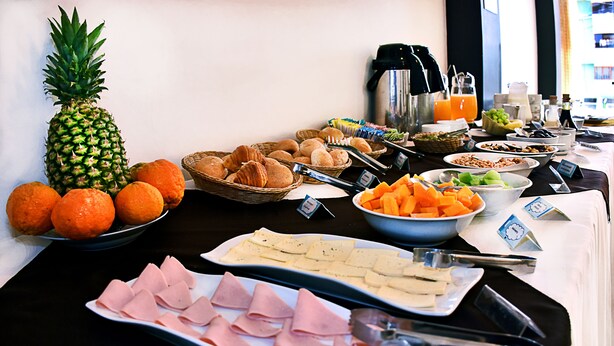 A buffet table with various food items including fruits, pastries, and meats.