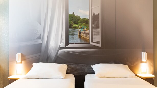 Habitación de hotel con una cama, dos mesitas de noche y una ventana que da a un cuerpo de agua y vegetación.