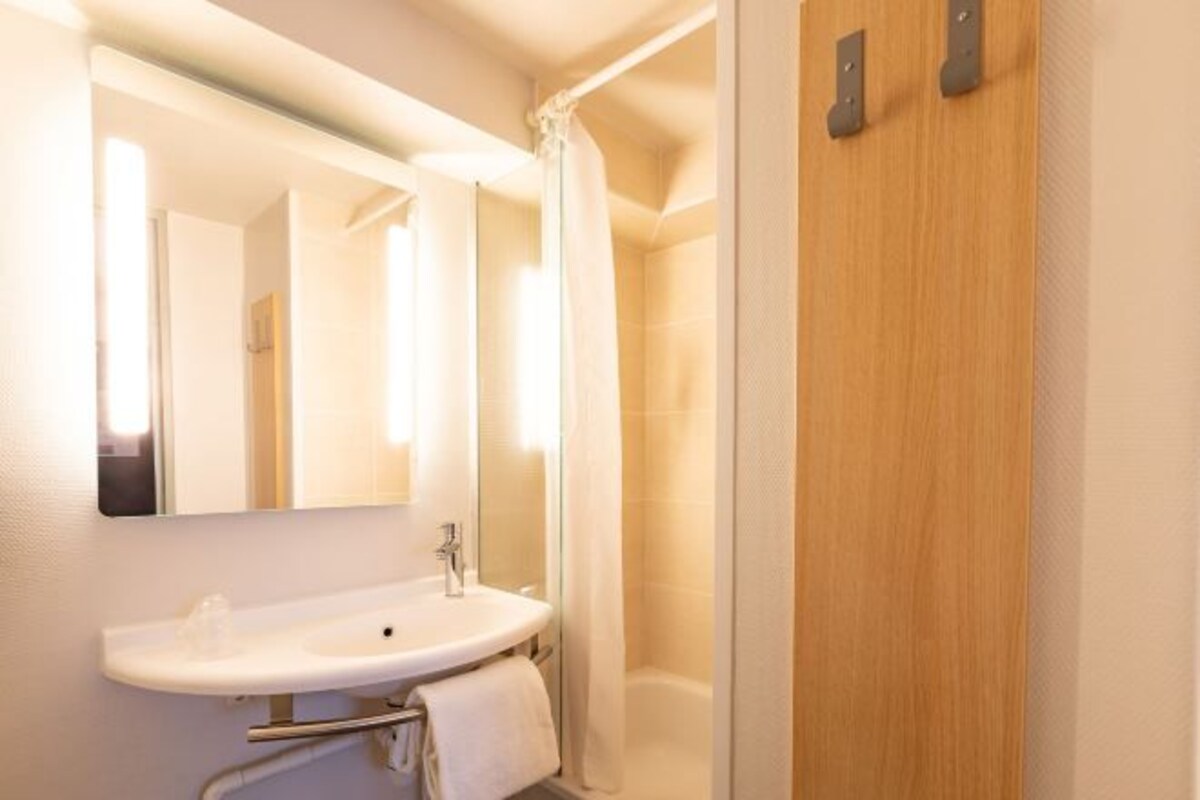 A bathroom with a sink, mirror, shower curtain, and wooden door.
