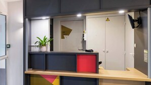 Mostrador de recepción con planta en maceta, detalle rojo y un letrero de advertencia en la puerta.
