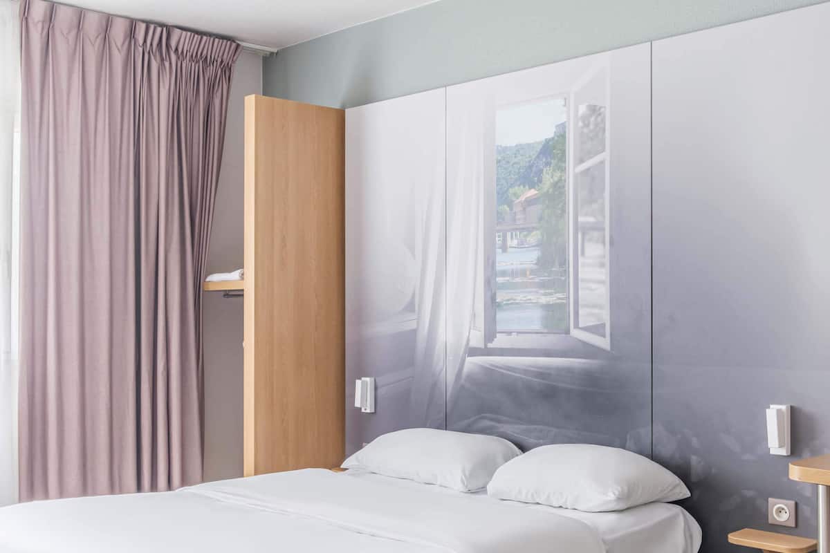 A bedroom with a bed, a wooden wardrobe, a window with a view, and a curtain.