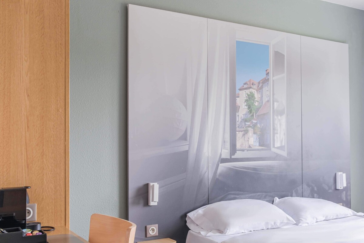 A hotel room with a large bed, a desk with a laptop, and a wall-mounted TV.