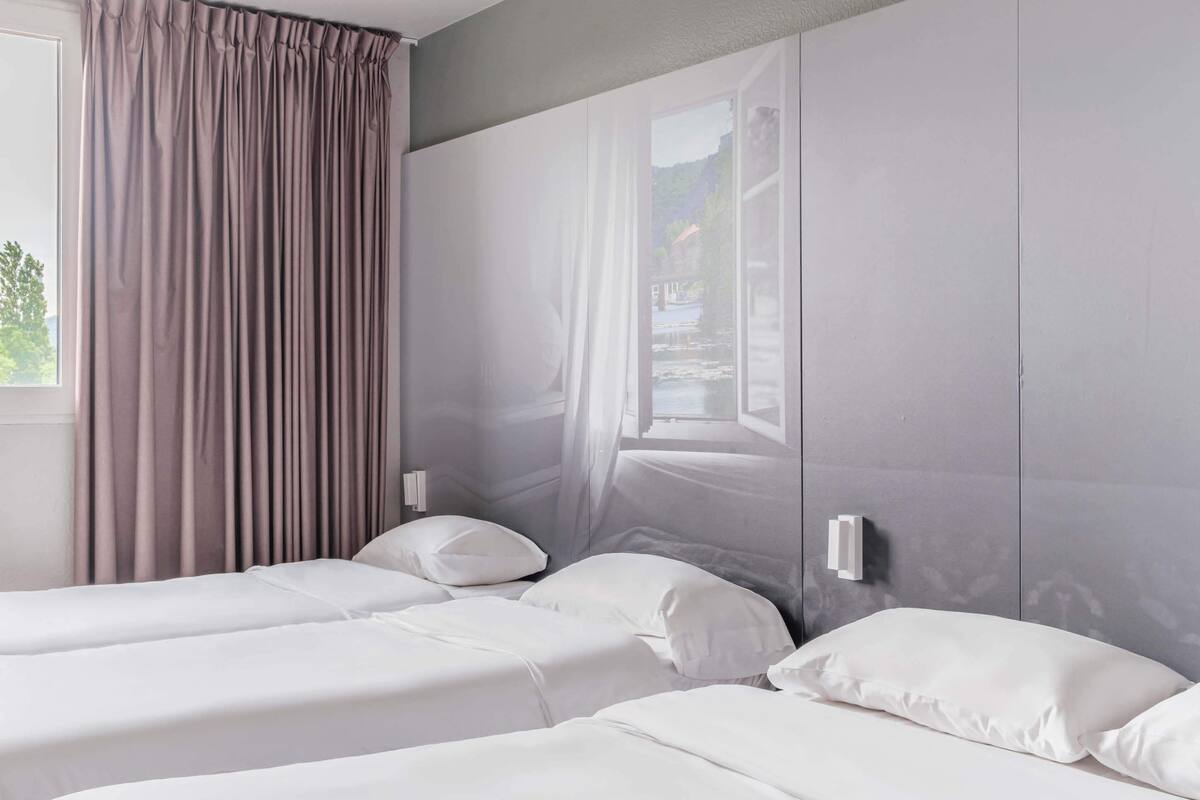 A hotel room with two beds, a large window with curtains, and a view of a body of water and mountains.
