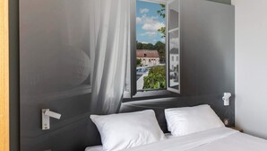 A bedroom with a bed, white pillows, a window with curtains, and a view of a building and trees.
