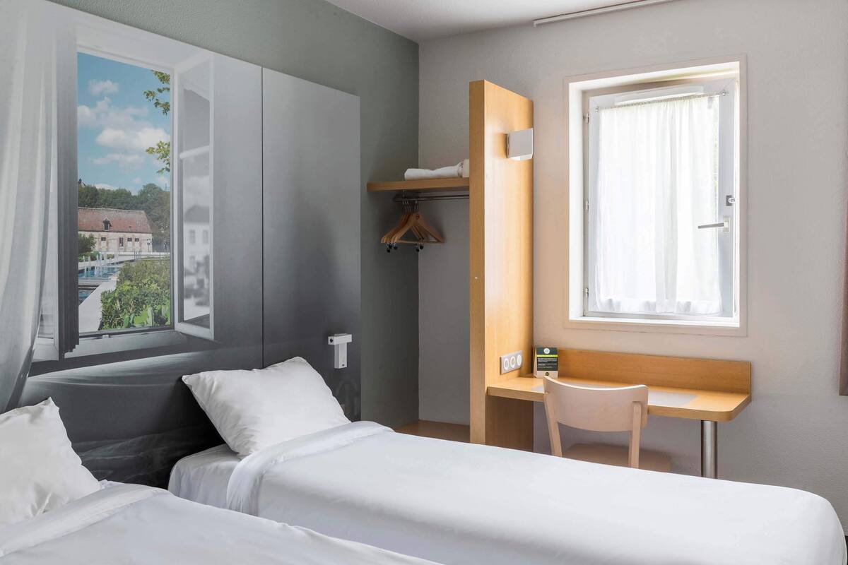 Ein Hotelzimmer mit Bett, Schreibtisch und einem fensterbepflanzten Fenster.