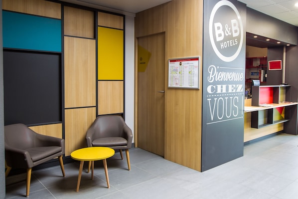 Zona de recepción de un hotel B&B con un panel de madera, una mesa amarilla, dos sillones de cuero y un mostrador de recepción.