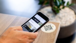 A smartphone displaying a hotel booking app with a QR code on a wooden surface.