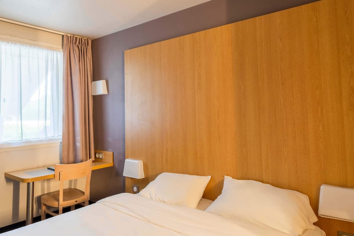 Une chambre d’hôtel comprenant un lit, un bureau, une chaise et une table de chevet avec une lampe.