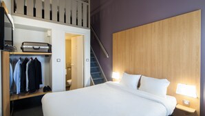 Een hotelkamer met een bed, een kast met kleren en een koffer, plus een trap.