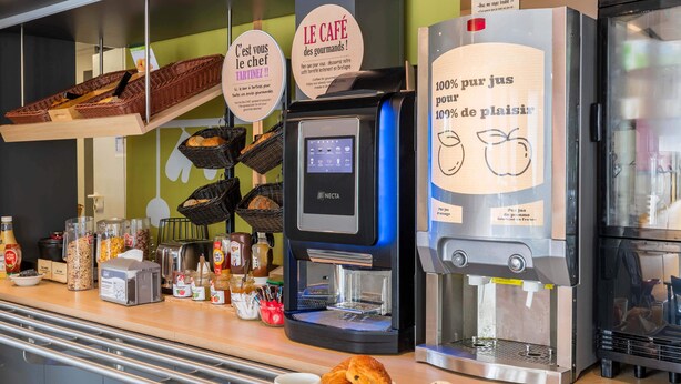 A breakfast counter with a coffee machine, a water dispenser, and a variety of breakfast items including croissants, eggs, and orange juice. - B&B HOTEL Troyes Barberey (La Chapelle-Saint-Luc)