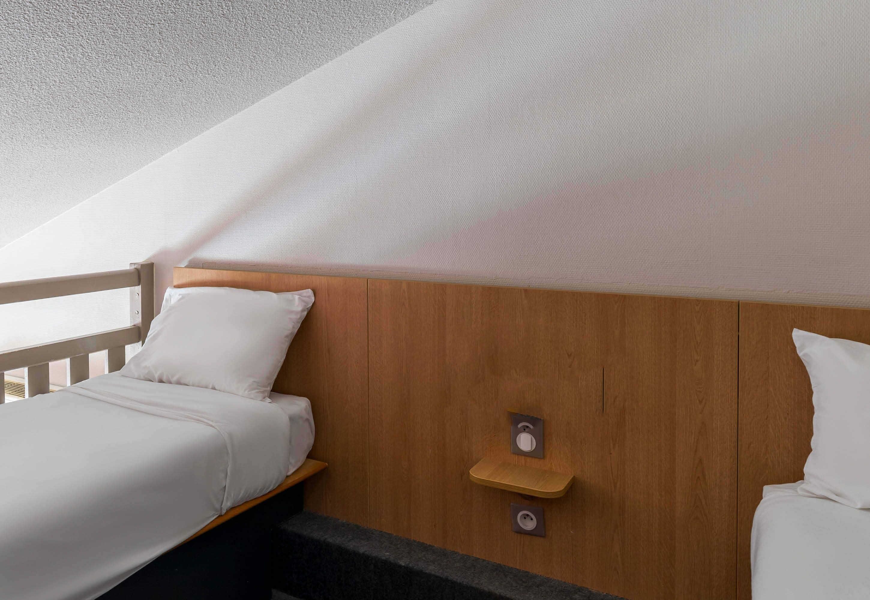 Une chambre avec deux lits, des têtes de lit en bois, une petite étagère en bois et un plafond à texture.