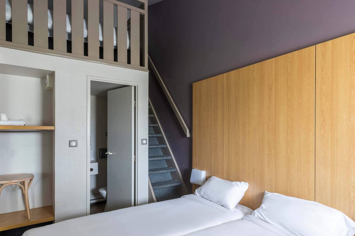Une chambre à coucher avec un lit, un bureau et une chaise. Un escalier mène à un niveau supérieur.