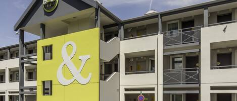 A B&B hotel with a distinctive yellow and white facade, multiple balconies, and a clear sky.