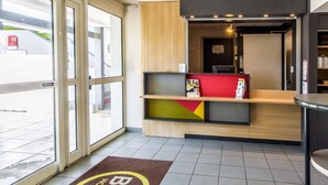 Een hotel receptie met een modern design, met een receptiebalie, een wachtruimte met een kleurrijke geometrische wand en een groot raam met uitzicht.