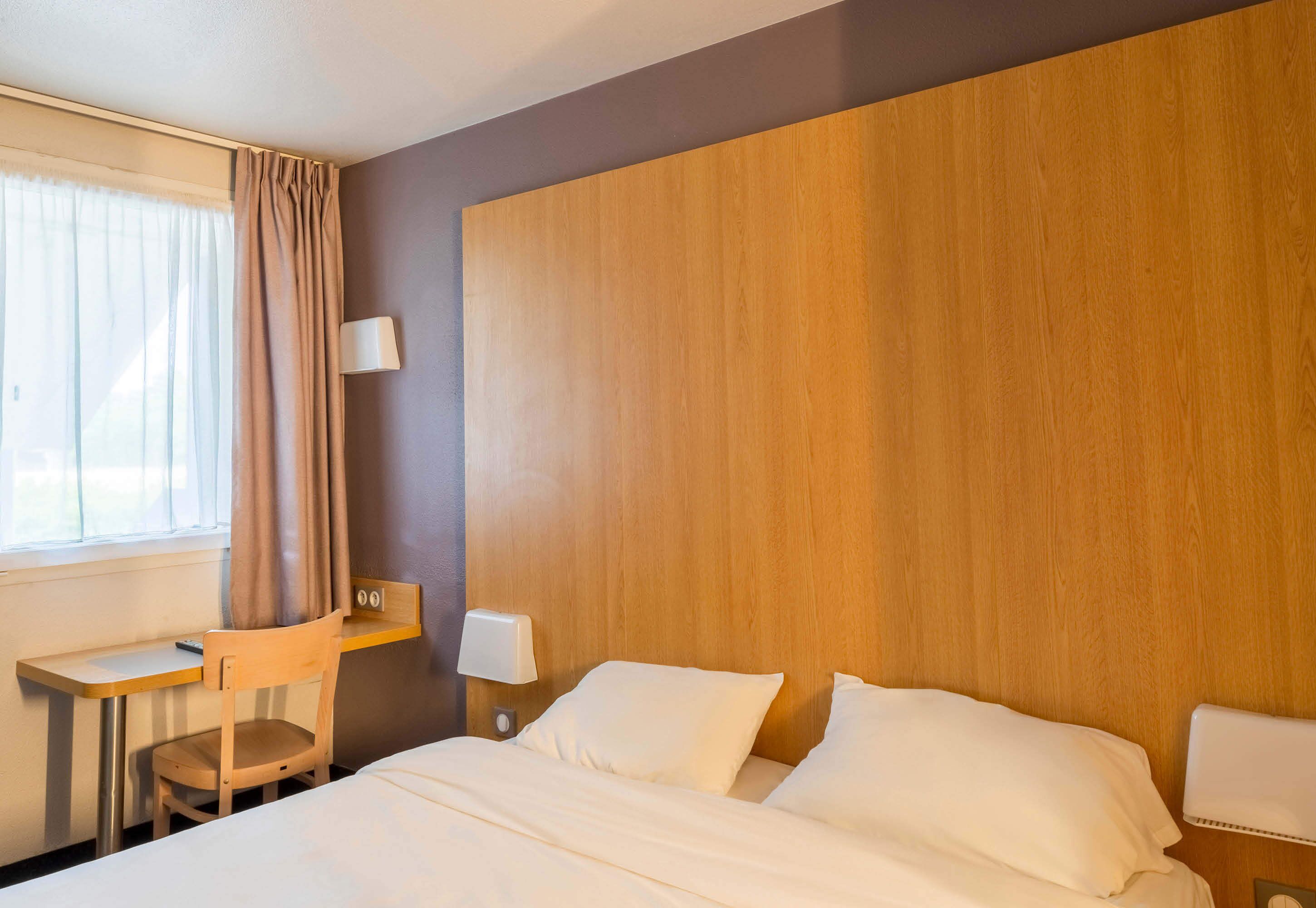 Een hotelkamer met een bed, een bureau, een stoel en een nachtkastje met een lamp.
