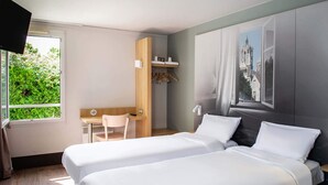 Habitación de hotel con dos camas, un escritorio, una silla, un armario y ventana con vistas a zonas verdes.
