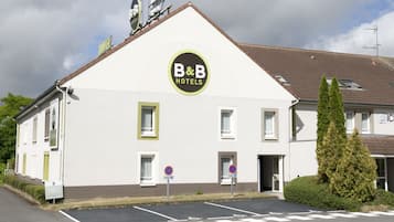 A B&B hotel with a white facade, a pitched roof, and a sign with the hotel's name. There are two parking spaces marked with 'no parking' signs.