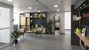 Un área de recepción moderna con un mostrador, zona de estar y plantas en macetas.