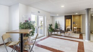 Een receptiegedeelte met een houten tafel en stoelen, een glazen deur en potplanten.