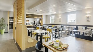 Een moderne cafetaria met meerdere tafels en stoelen, een koffiehoek en een potplant.