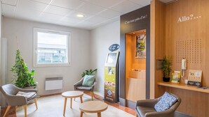 Een receptiegedeelte met een houten bureau, een zithoek met stoelen en tafels, een plant en een raam met uitzicht op buiten.